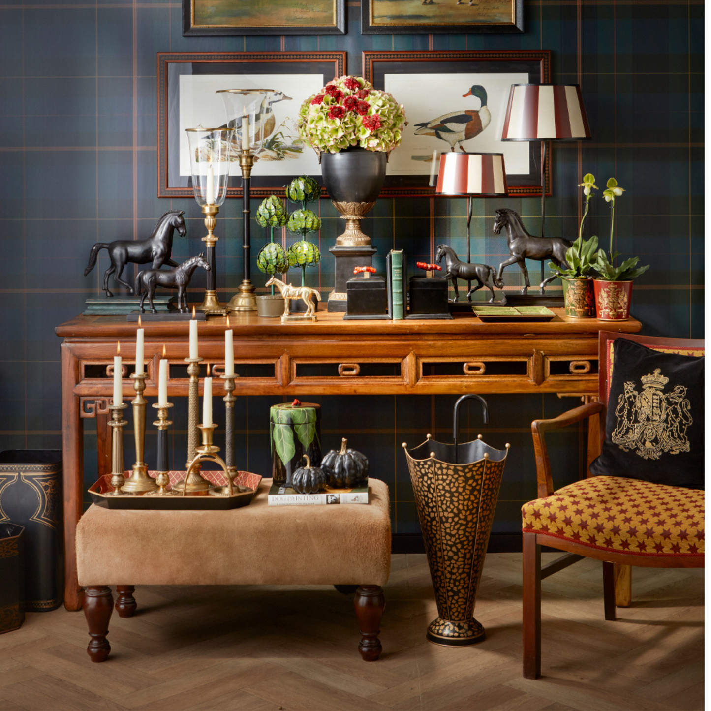 Stilvolles Interior-Arrangement mit antikem Holztisch, Kerzenhaltern aus Messing, schwarzen Pferdefiguren, floralem Lampenschirm und Schirmständer mit Leopardenmuster – britisch-elegantes Wohnambiente.