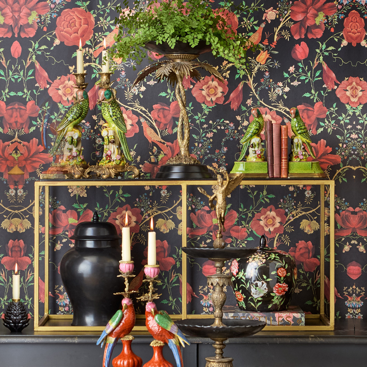 Exotische Dekoarrangements mit Papageienkerzenhaltern, grünen Vogelbuchstützen, goldener Palmenetagere und floral verzierter Tapete – ausdrucksstarkes Interior mit tropischen Akzenten und barockem Flair.